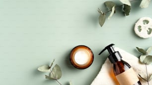 SPA Kosmetikprodukte Branding Mockup. Klare Pump-Shampoo-Flasche auf Handtuch, Feuchtigkeitscreme-Cremeglas, Luffa, Eukalyptusblätter auf grünem Hintergrund. Natürliches pflanzliches Schönheitsproduktdesign.