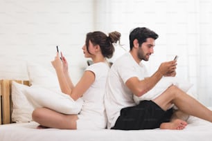 Millennial couple in quarrel, lying in bed back to back, using cellphones