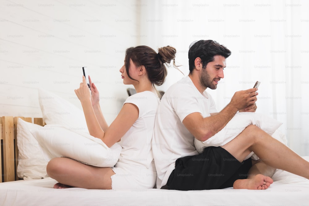 Millennial-Paar im Streit, liegt Rücken an Rücken im Bett, benutzt Handys