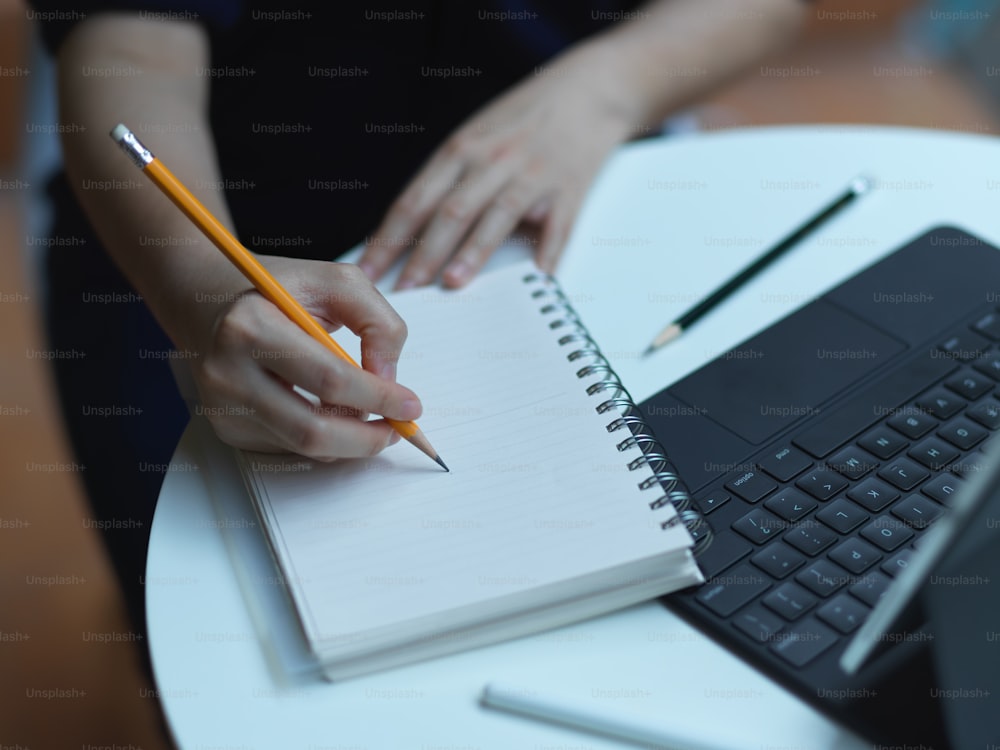 Vista de cerca de la escritura a mano femenina en un cuaderno en blanco mientras se trabaja con una tableta digital