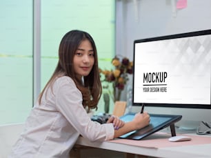 Portrait of female office worker smiling to camera while working with drawing tablet and computer