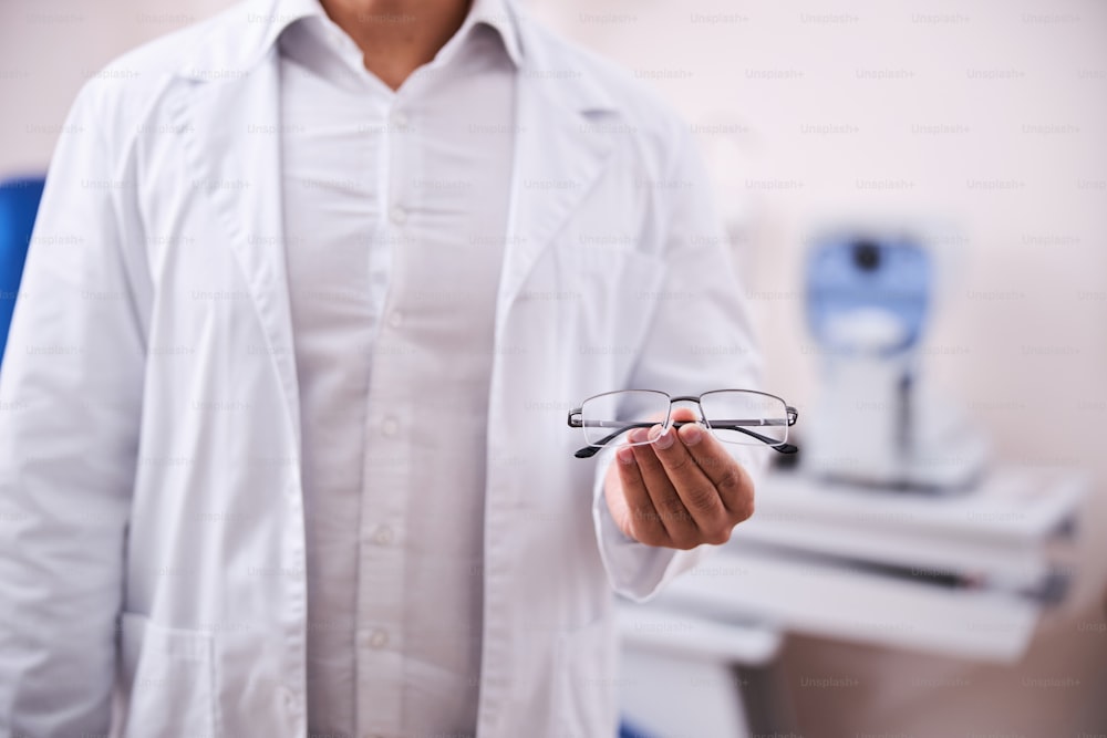Cropped photo of an optician holding a new pair of prescription glasses in front of the camera
