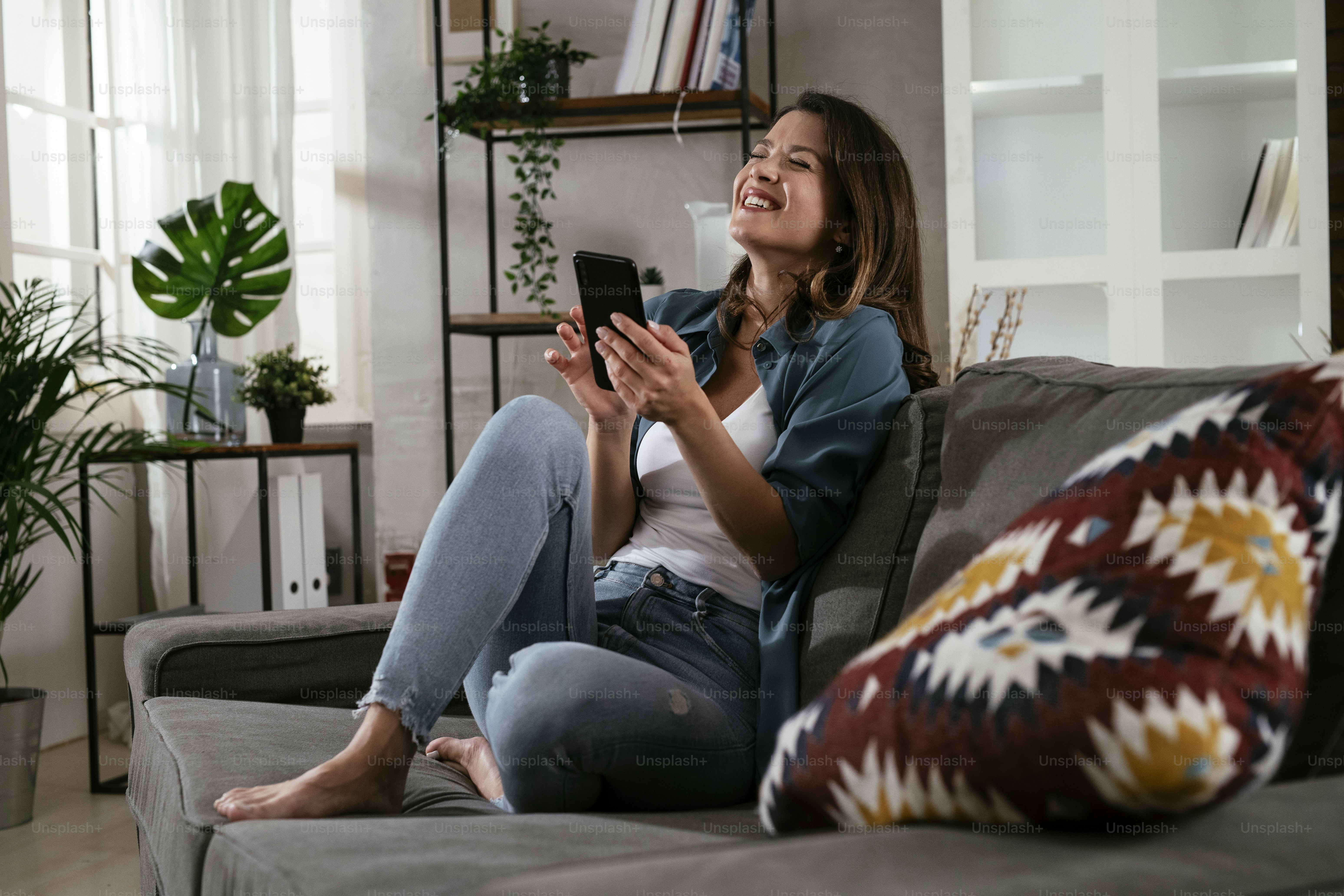 Happy young woman using the phone at home. Excited woman enjoying in the living room.