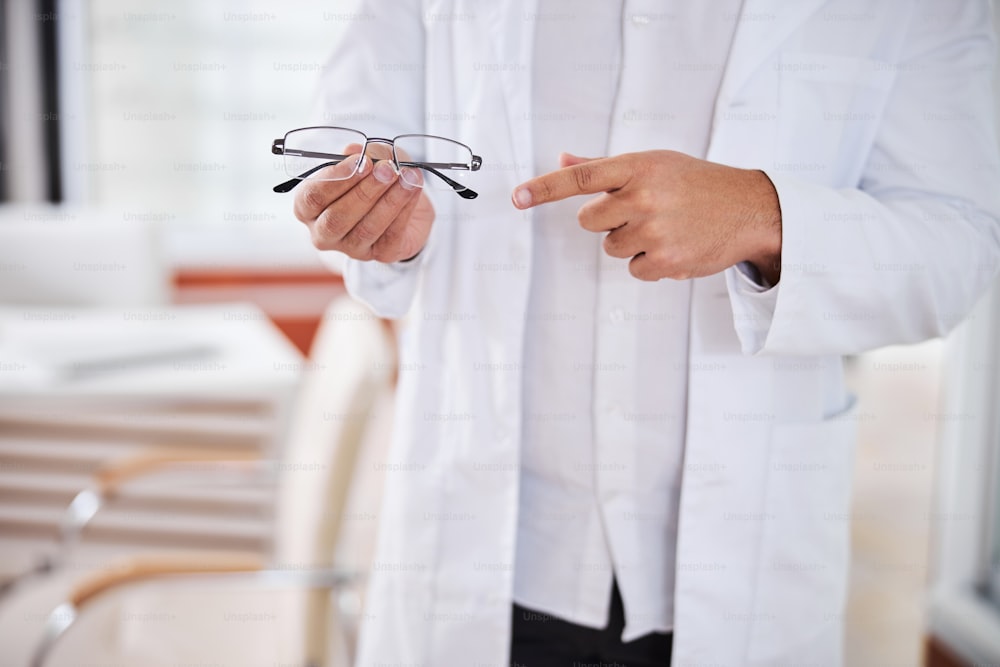 Beschnittenes Foto eines männlichen Optikers, der mit dem Zeigefinger auf eine neue Brille zeigt