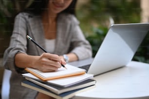 Cropped shot of businesswoman working on laptop computer and making notes in a notebook.
