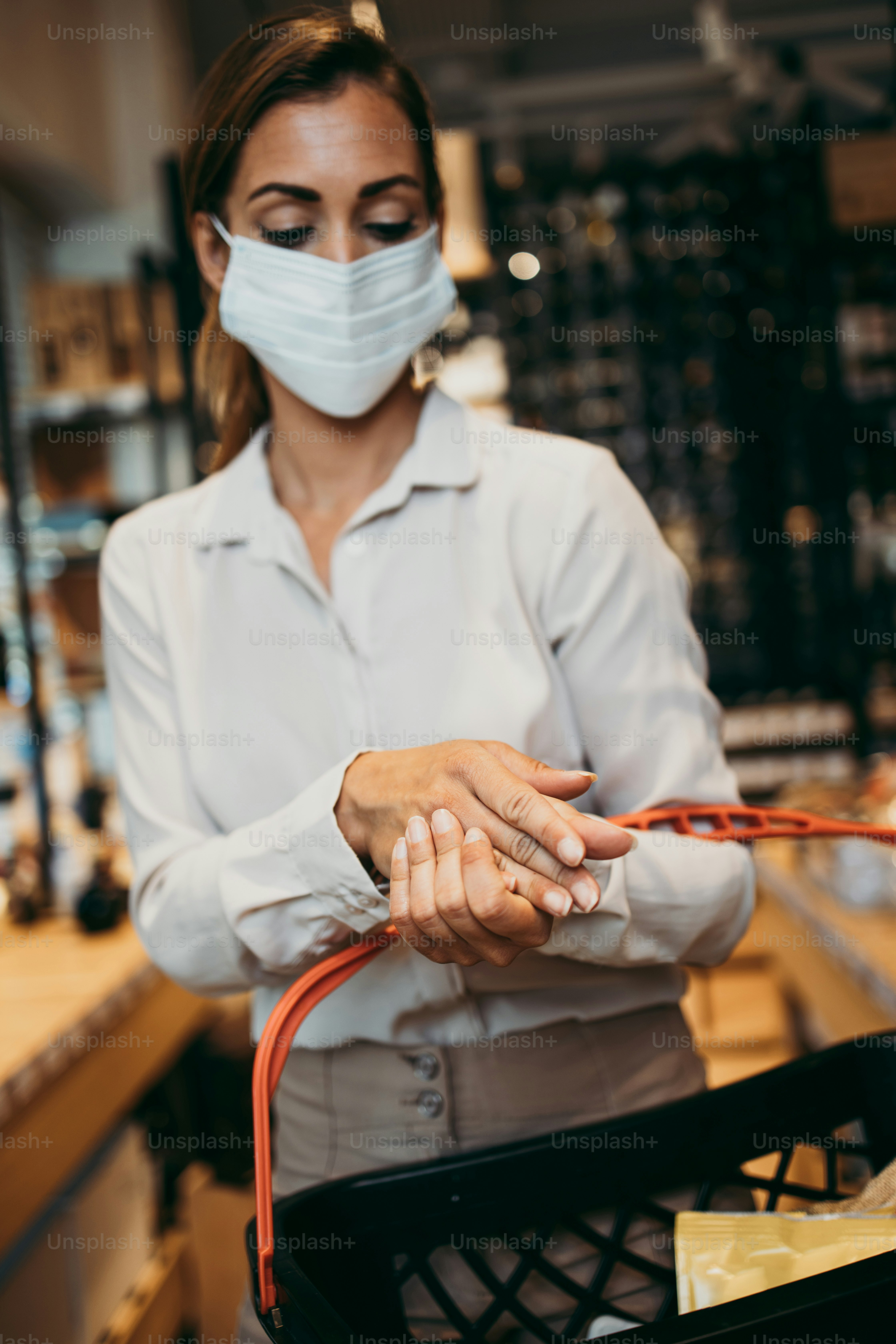 Beautiful young and elegant woman with face protective mask and gloves buying healthy food and drink in a modern supermarket or grocery store. Pandemic or epidemic lifestyle and consumerism concept.