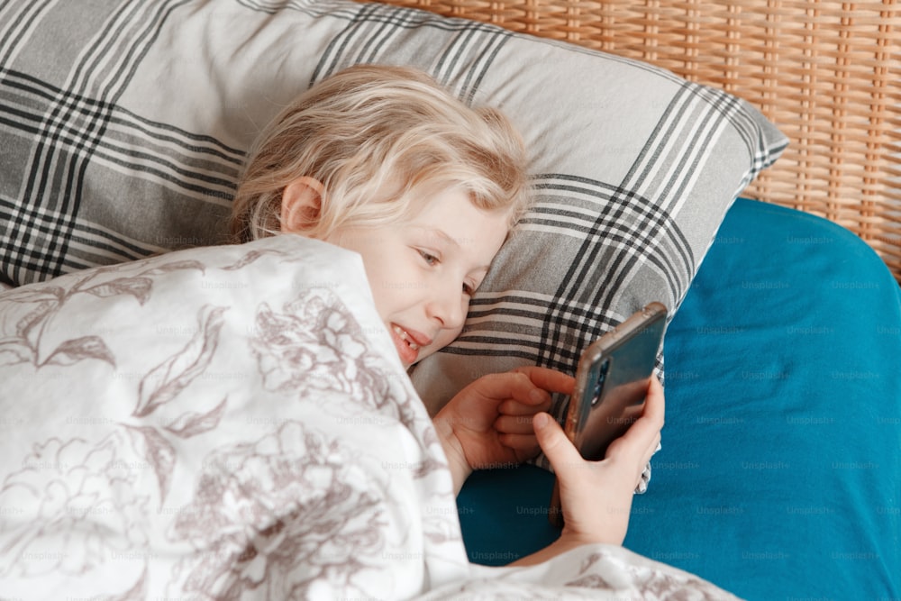 Jolie fille allongée dans son lit le matin et envoyant des SMS sur les réseaux sociaux sur son téléphone portable. Enfant enfant tapant des messages sur un téléphone portable. Discutez avec des amis en ligne sur Internet. Chat vidéo.