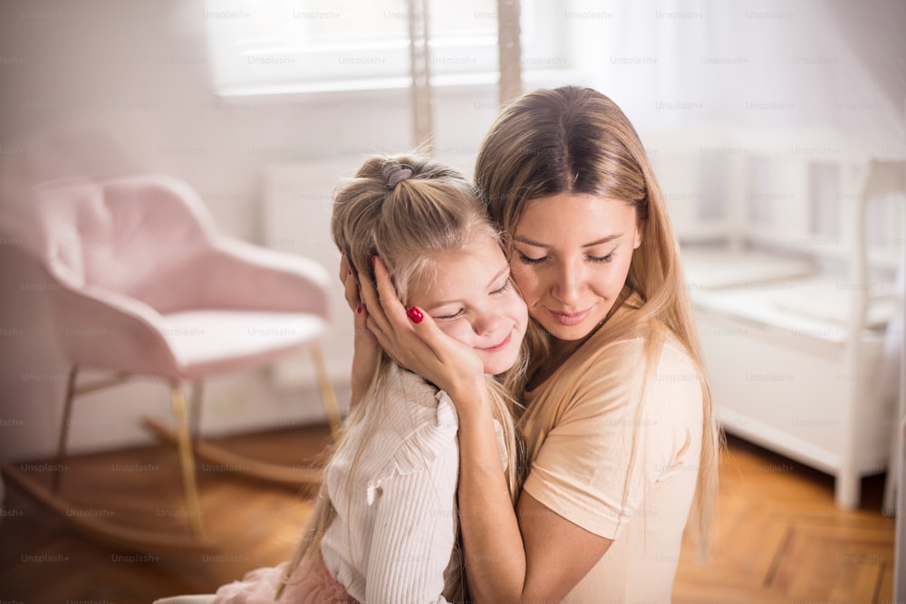 Portrait of mother and daughter in bedroom. Mom and kid in hug.