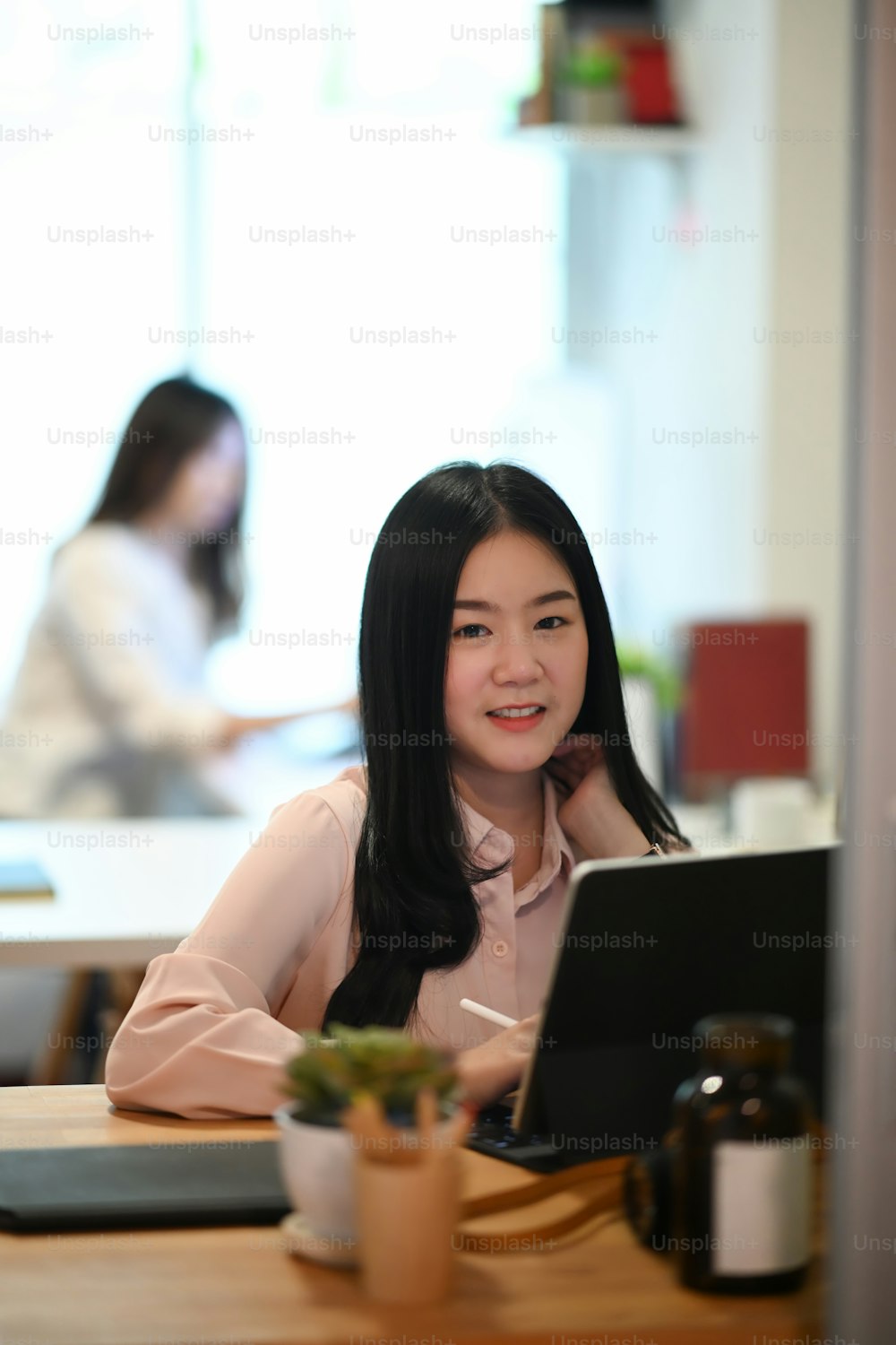 Porträt einer jungen Grafikdesignerin, die in einem modernen Büro sitzt und in die Kamera lächelt.
