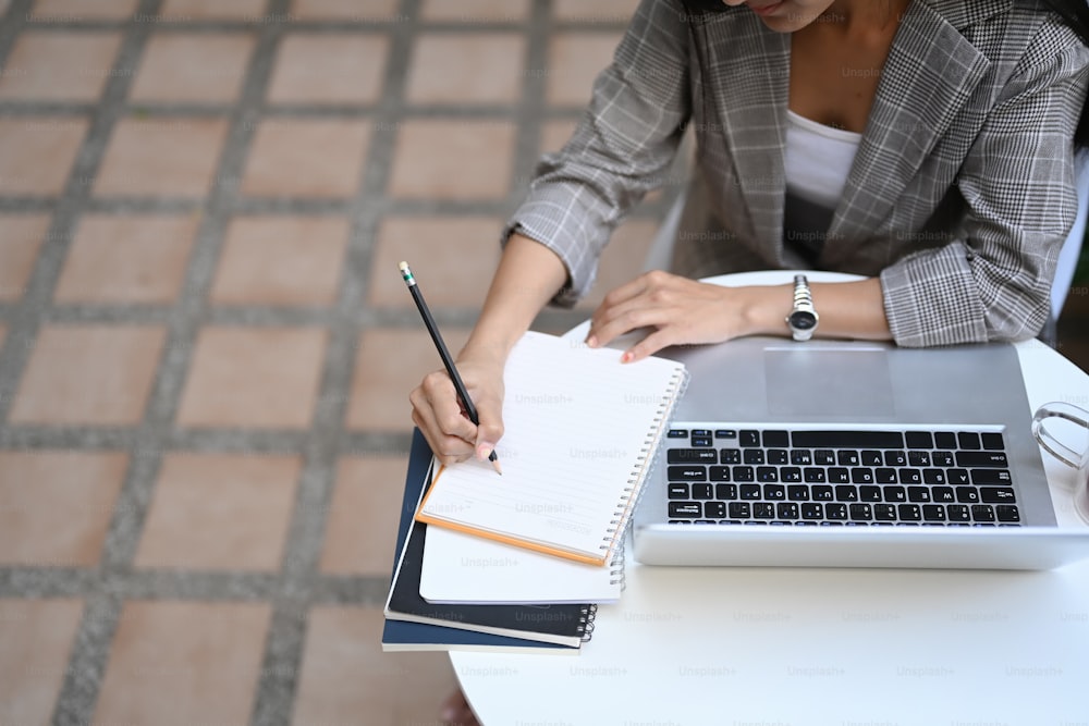 Cropped shot of businesswoman working with laptop computer and writing on empty notebook.