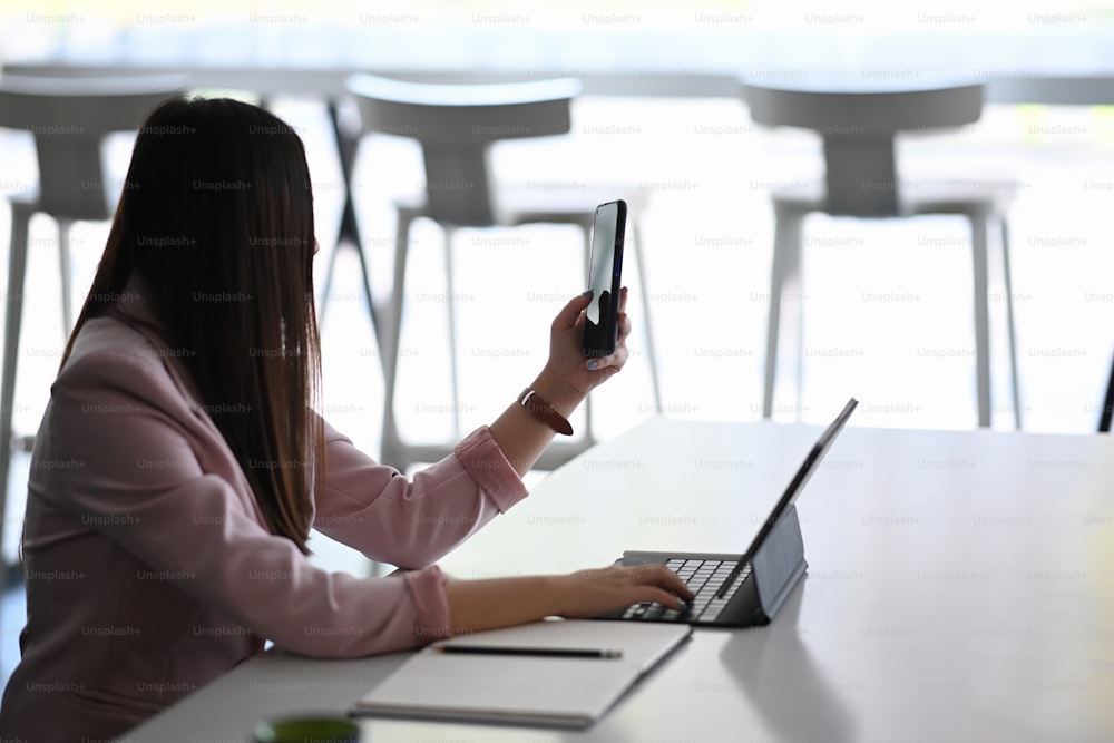 Empresária que trabalha com tablet na mesa do escritório e faz chamada de vídeo com seus colegas.