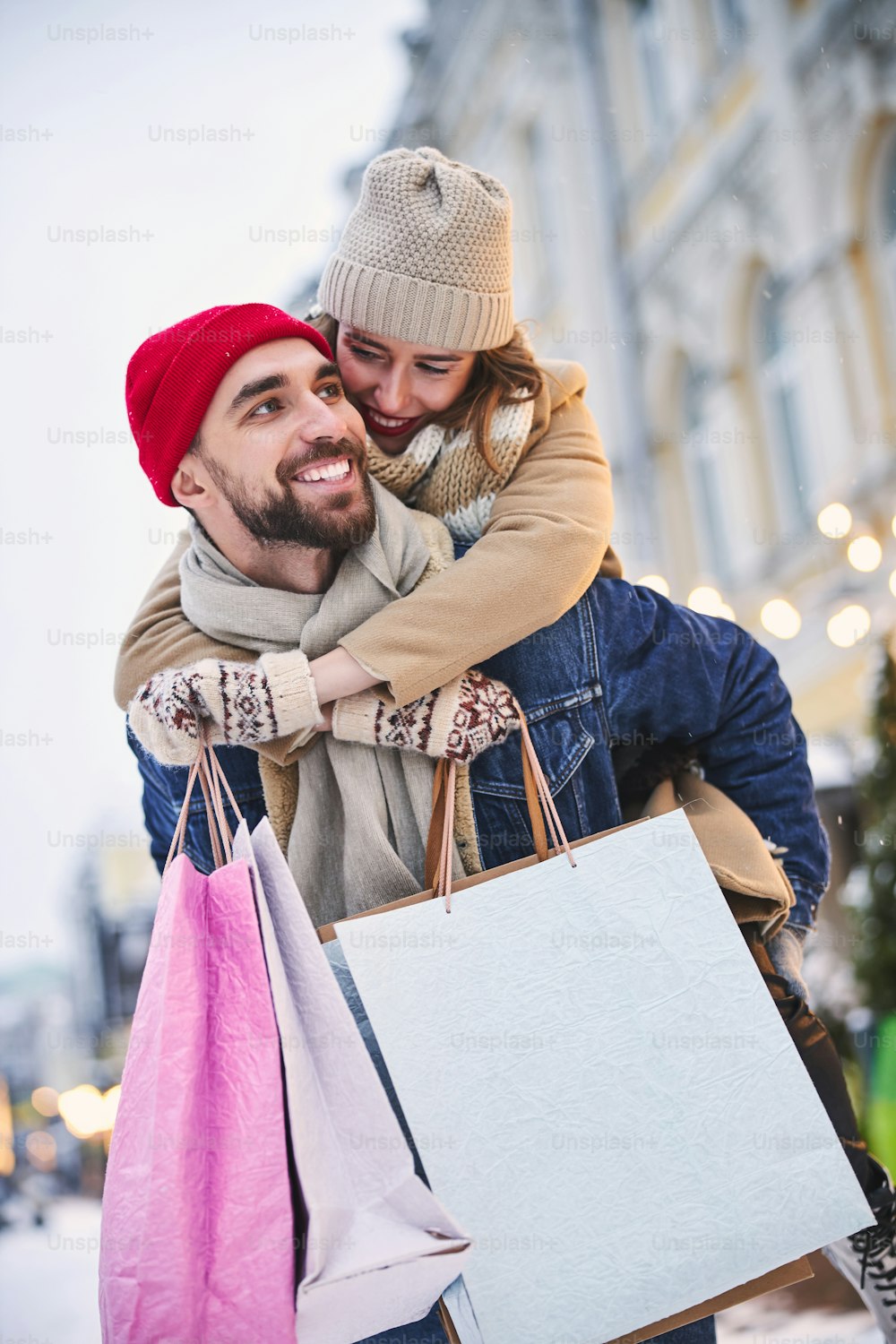 행복한 수염 난 남자는 야외에서 쇼핑을 한 후 걷는 동안 종이 봉지와 그의 여자 친구를 들고 있다