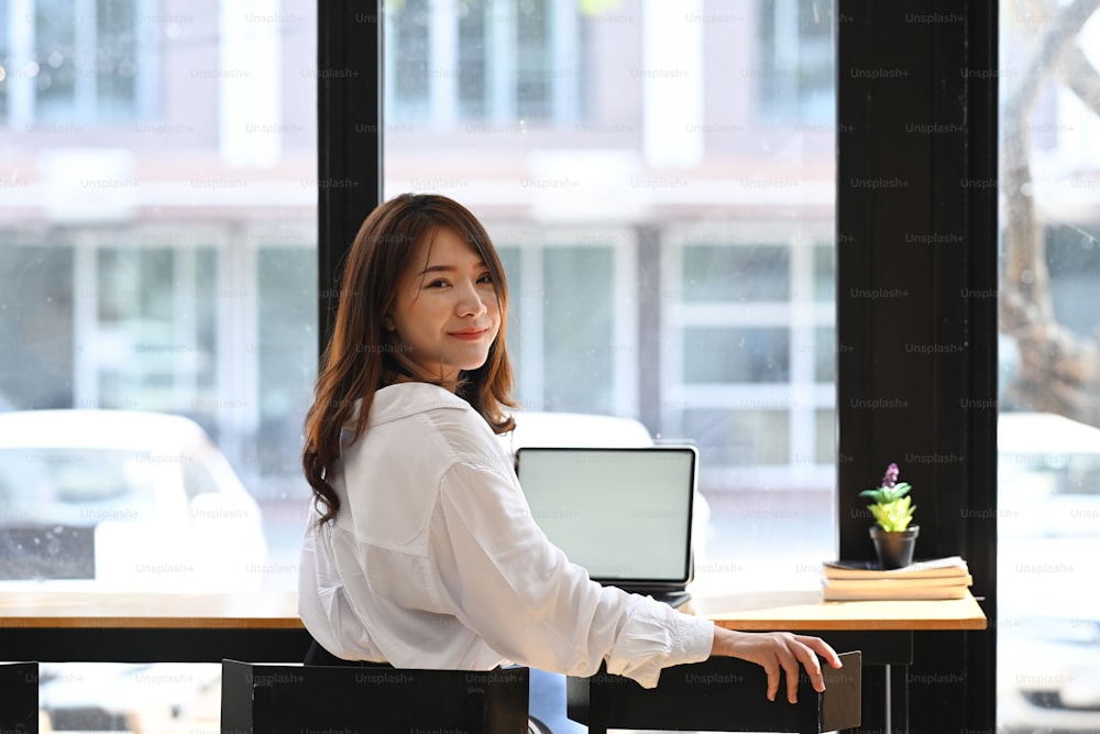 Confident businesswoman sitting near window and looking at camera.