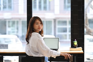 Confident businesswoman sitting near window and looking at camera.