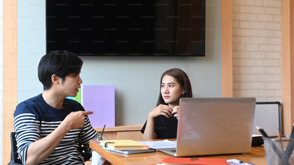 Dois jovens empresários trabalhando juntos em laptop e analisando relatórios na mesa do escritório.