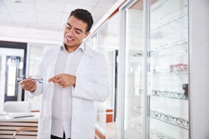 Consultor de gafas sonriente y alegre señalando con el dedo índice un par de gafas en sus manos