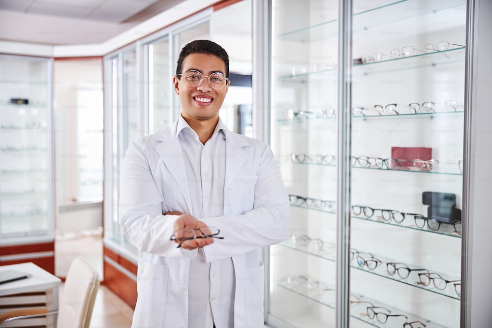 Front view of a good-looking eyewear consultant holding a pair of spectacles in his hands