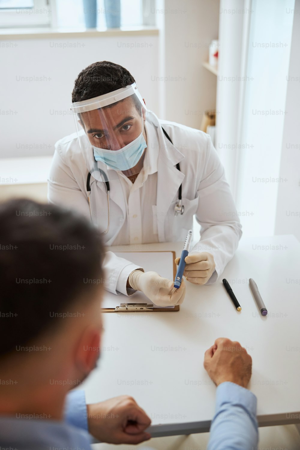 Retrato de cerca del terapeuta valiente profesional con el estetoscopio en el hombro hablando con el paciente en la habitación interior de la clínica médica