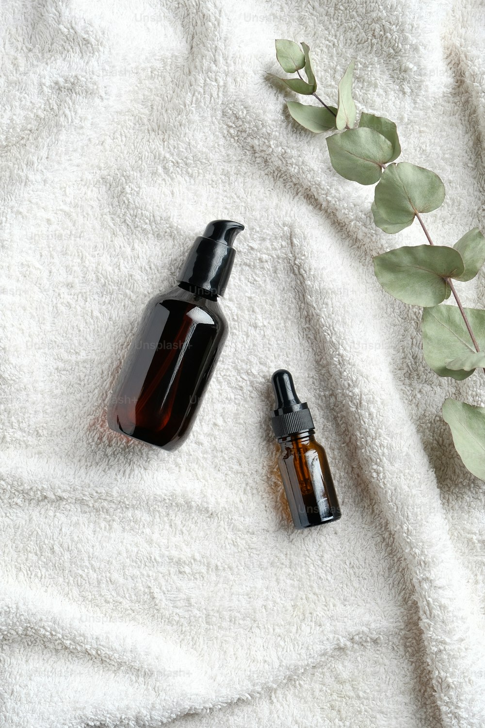 SPA Naturkosmetik-Set. Serum und ätherisches Öl mit Eukalyptusblatt auf weißem Handtuch im Badezimmer. Flache Lage, Draufsicht.