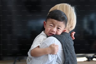 Mother holding her crying son living room at home.