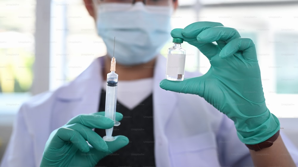 실험실에서 보호 마스크를 쓴 여성 의사 또는 과학자의 클로즈업 손은 약 백신과 주사기를 들고 있습니다.