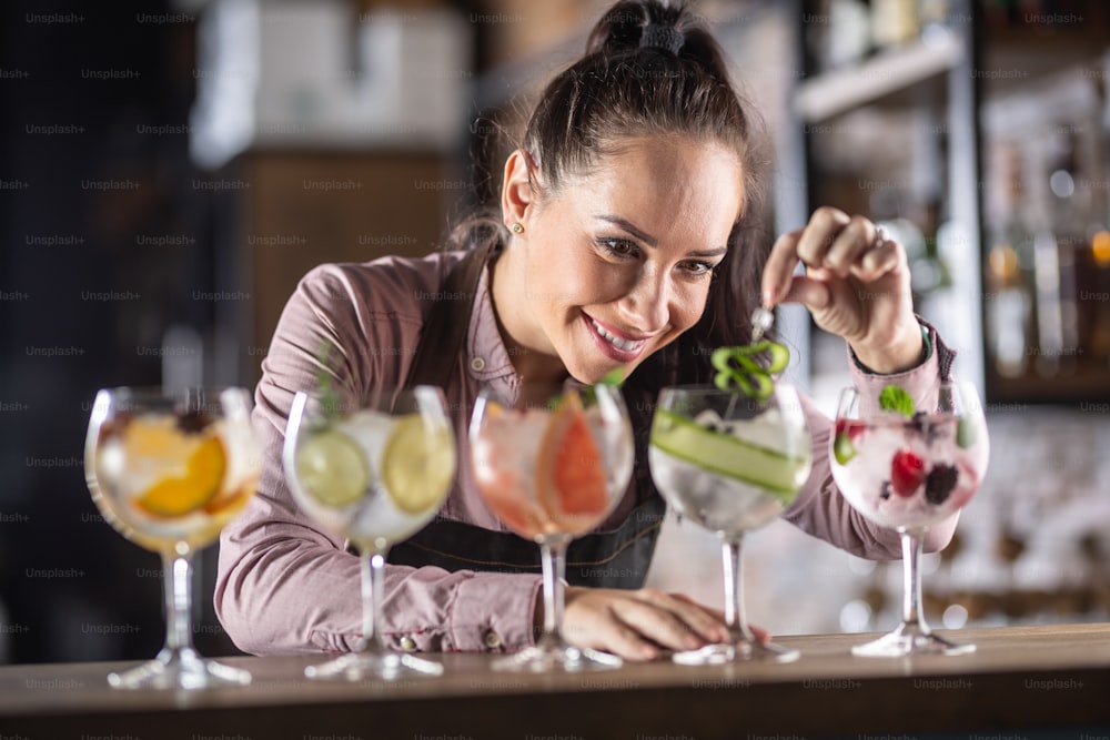 Ampia selezione di bevande a base di gin tonic preparate su un bancone da una barista di bell'aspetto.
