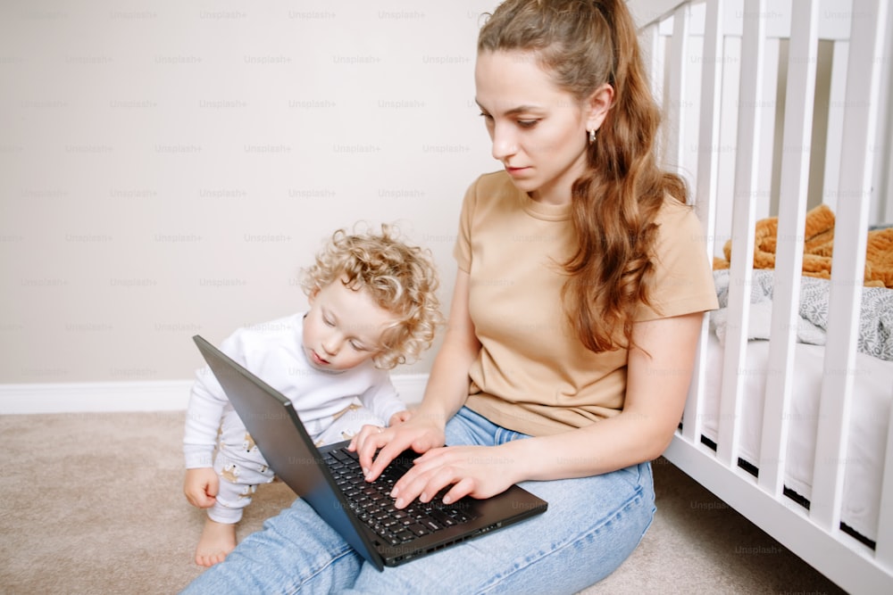 Caucasian mother with baby working on laptop from home. Workplace of freelance business woman with kid toddler. Video chat call. Stay at home single mom earning money at distant job online.