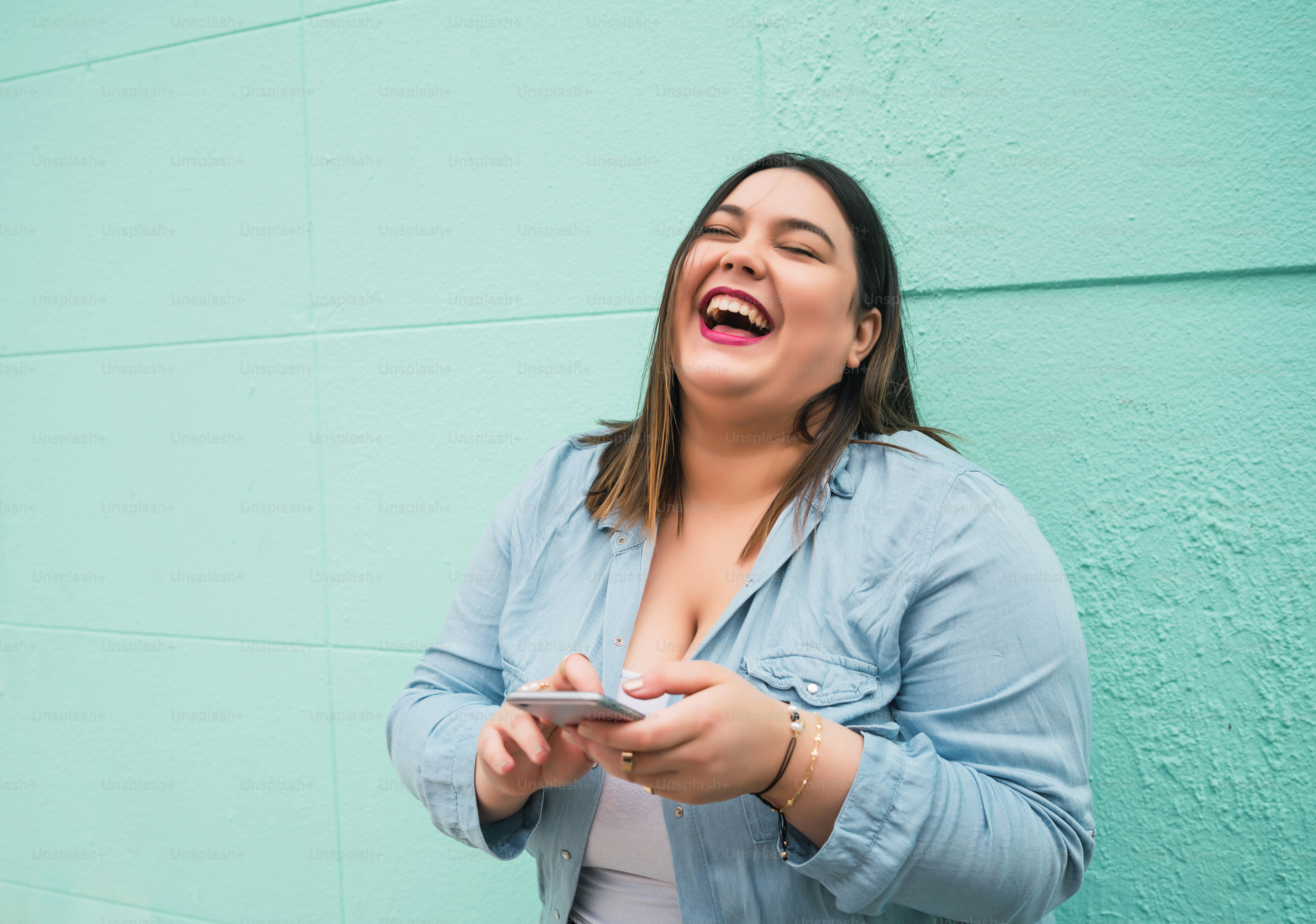 야외에서 휴대폰으로 문자 메시지를 입력하면서 웃고 있는 젊은 플러스 사이즈 여성의 초상화. 기술 개념입니다.