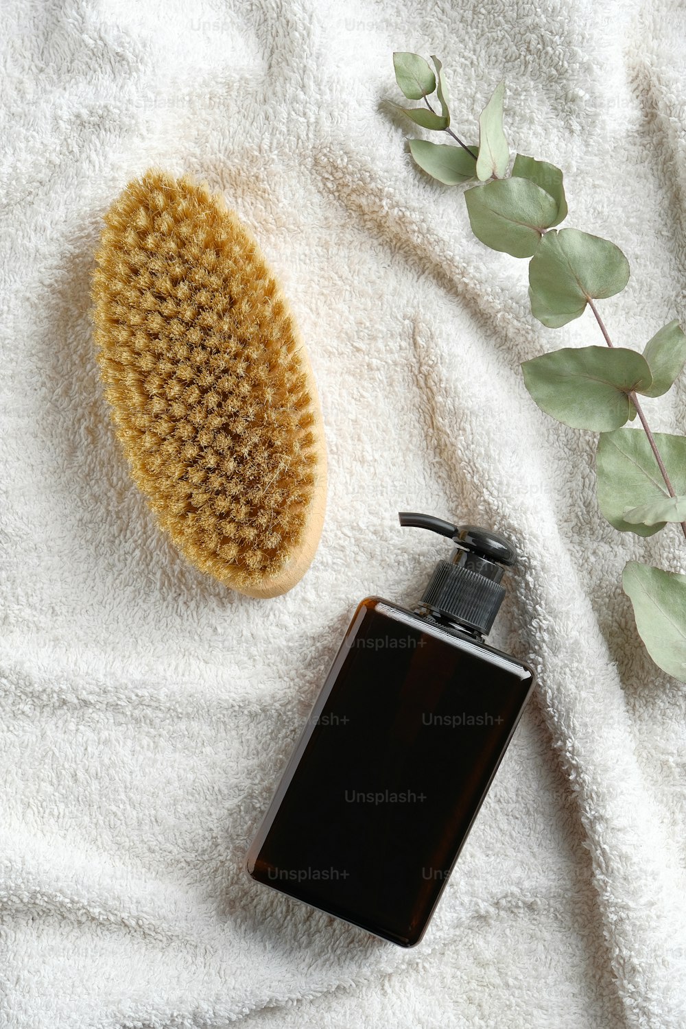 Dry brush, green glass lotion bottle and eucalyptus leaf on white towel in bathroom. SPA natural organic cosmetic products set. Body care, cellulite treatment concept.