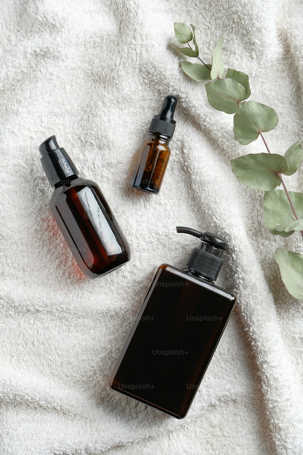Amber glass cosmetic bottles set and eucalyptus leaf on white towel. SPA bathroom natural cosmetics. Flat lay, top view