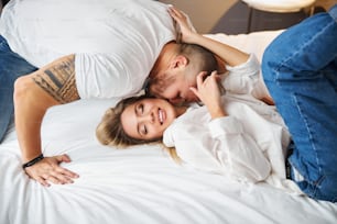 Smiling happy lovely young blonde Caucasian woman being kissed by her loving husband in bed