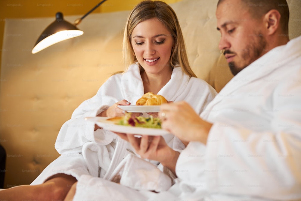 Smiling pretty lady and a serious handsome bearded young man looking at the food on their plates