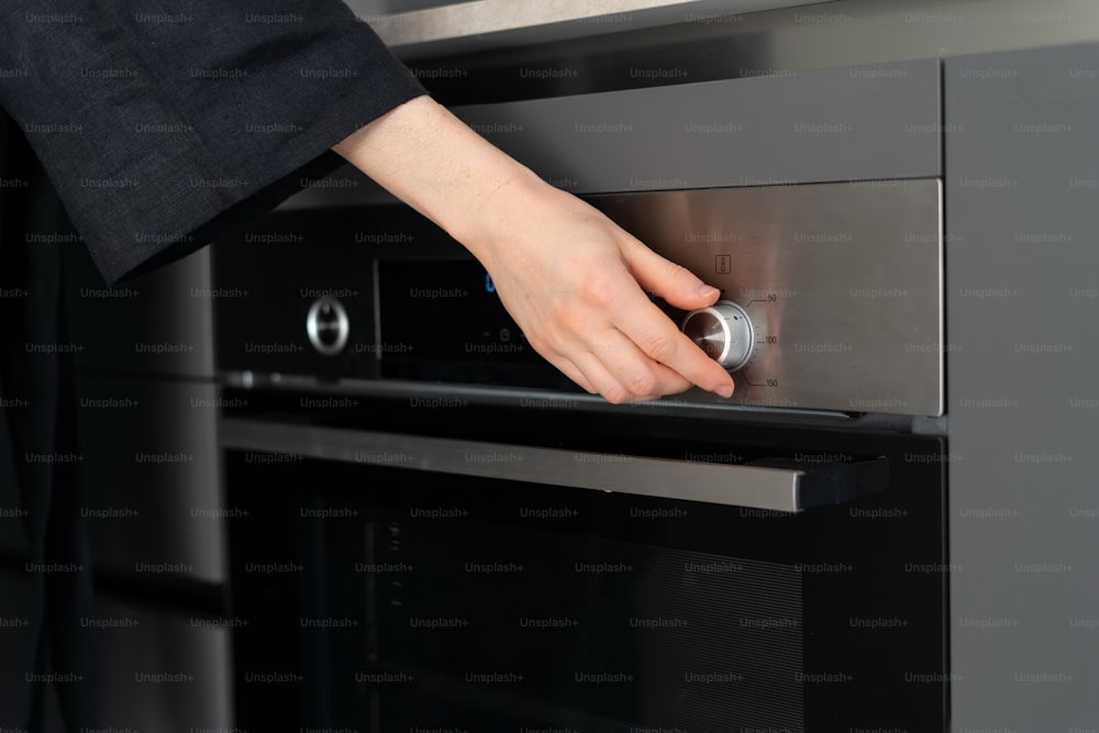 Cropped view of woman hand regulate temperature and switch program at modern built in oven appliance, cooking homemade food, standing on contemporary kitchen