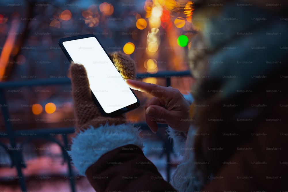 Primer plano de una mujer al aire libre en el parque de la ciudad en invierno usando aplicaciones de teléfonos inteligentes por la noche.