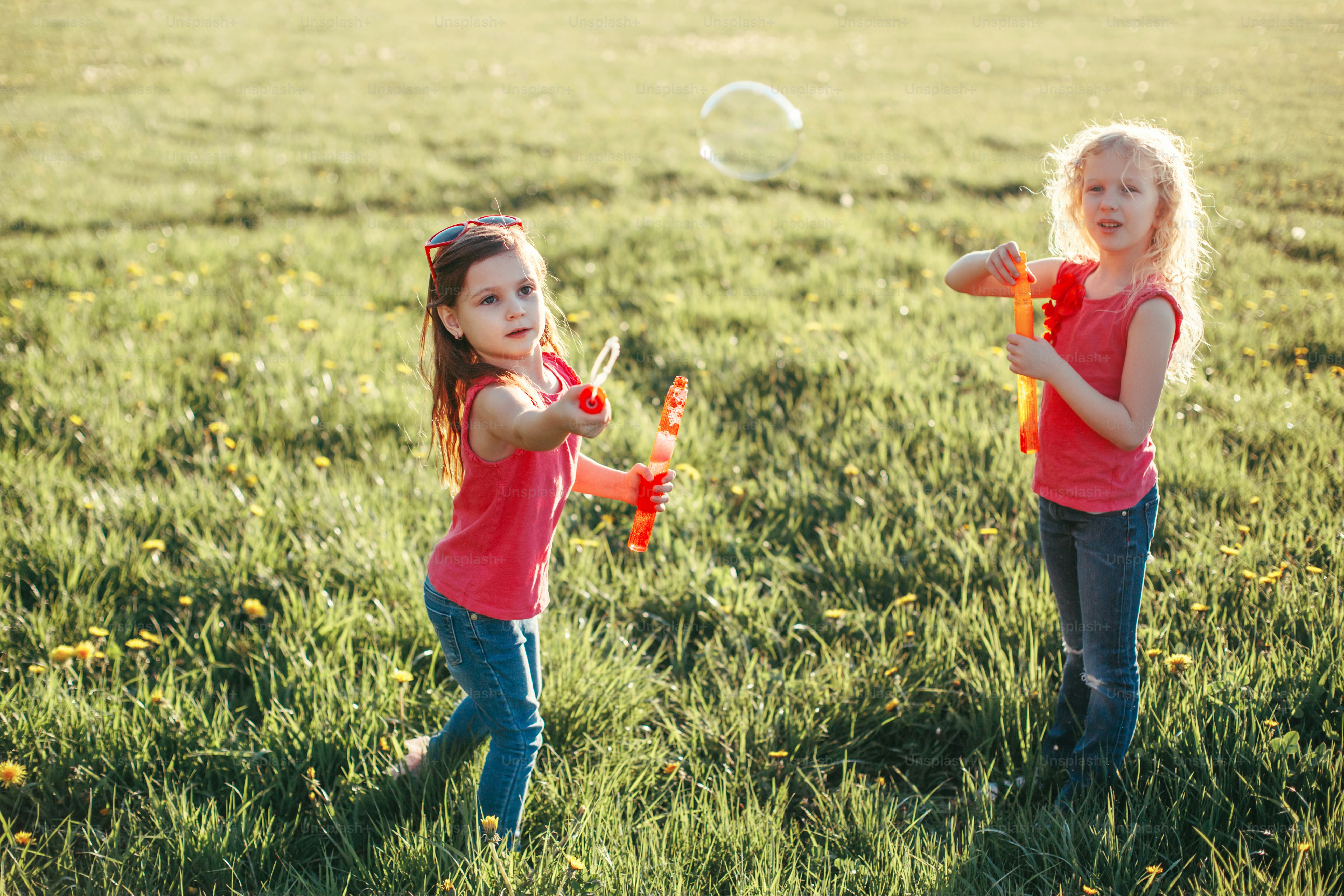 Happy Caucasian girls blowing soap bubbles in park on summer day. Kids ...
