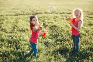 Des filles caucasiennes heureuses soufflant des bulles de savon dans un parc un jour d’été. Les enfants s’amusent à l’extérieur. Authentique moment magique d’enfance heureuse. Lifestyle activité saisonnière pour les enfants.