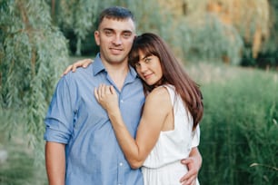 Beautiful married couple man woman in love. Husband and wife hugging in park on summer day at sunset. Togetherness and happiness. Authentic real people family outdoor.