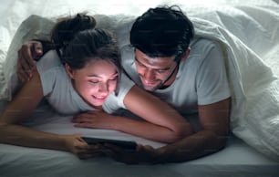 Close up Young Sweet Couple on Bed Watching Something on Tablet Gadget, relaxing in bedroom.