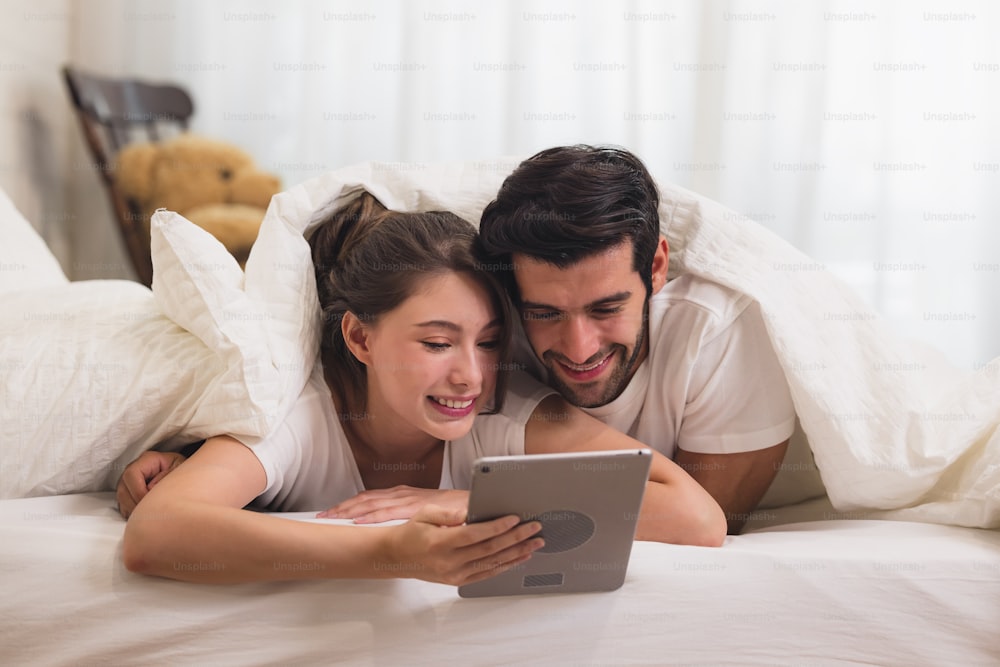 Close up Young Sweet Couple on Bed Watching Something on Tablet Gadget, relaxing in bedroom.
