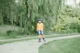 헬멧을 쓰고 헬멧을 쓴 행복한 미소를 짓고 있는 십대 초반 소년은 여름날 공원의 도로에서 롤러 스케이트를 타고 있다. 계절에 따라 야외 어린이 활동 스포츠. 건강한 어린 시절의 생활 방식.