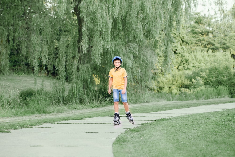 Happy smiling Caucasian preteen boy in helmet riding roller skates on road in park on summer day. Seasonal outdoor children activity sport. Healthy childhood lifestyle.