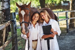いつでも喜んでお手伝いします。昼間に農場で屋外で馬を検査する2人の女性獣医。