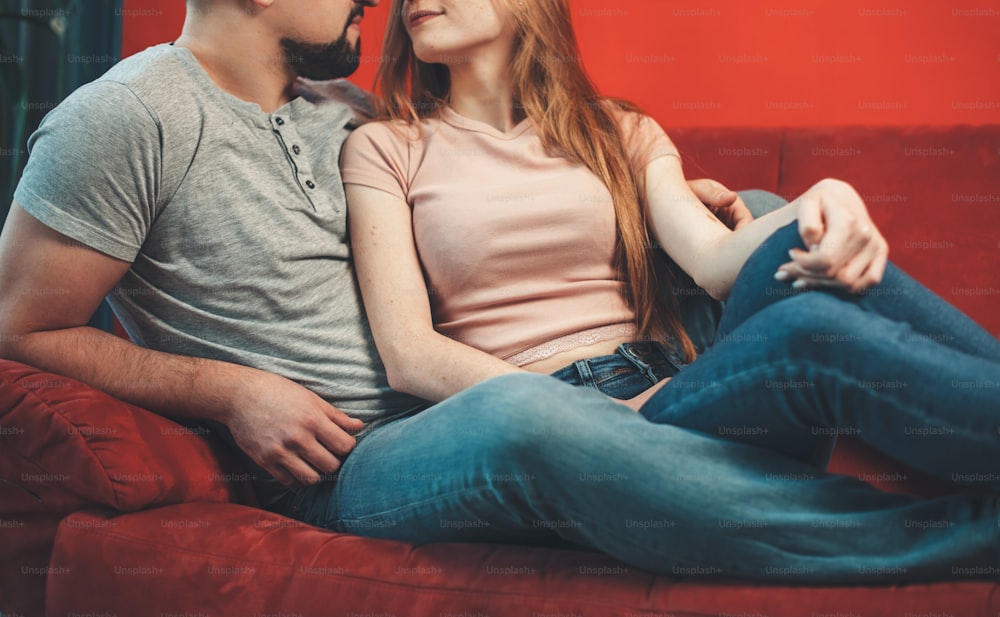 Adorable couple lying on a red couch and embracing while dating together the valentines day