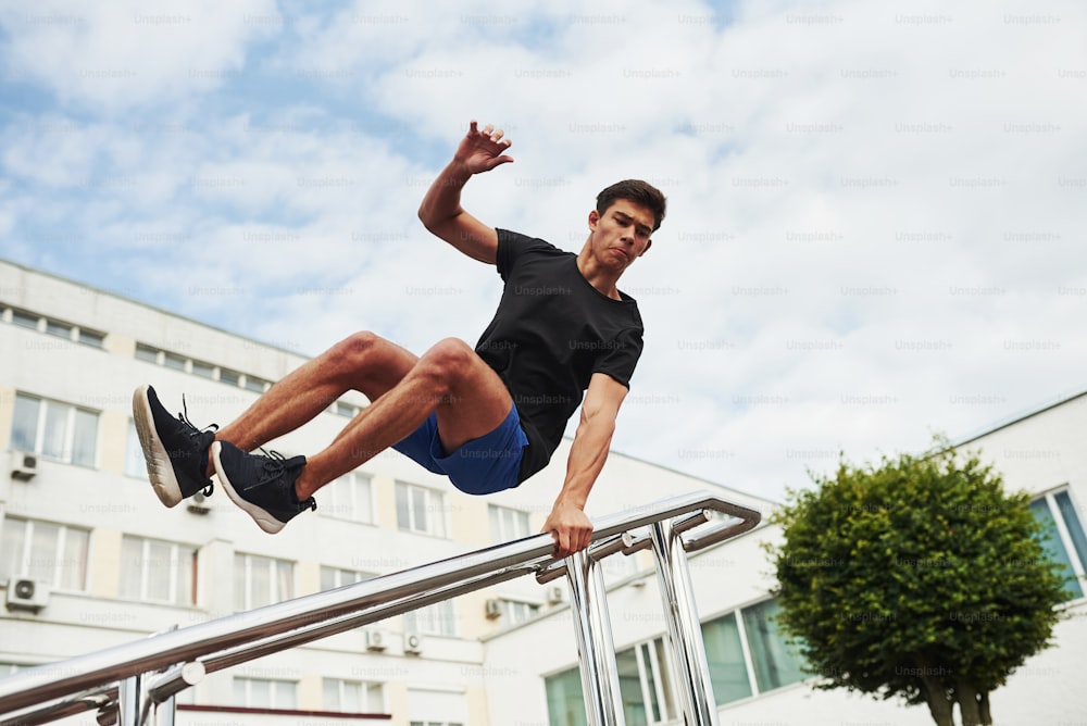 Silver colored railings. Young sports man doing parkour in the city at sunny daytime.