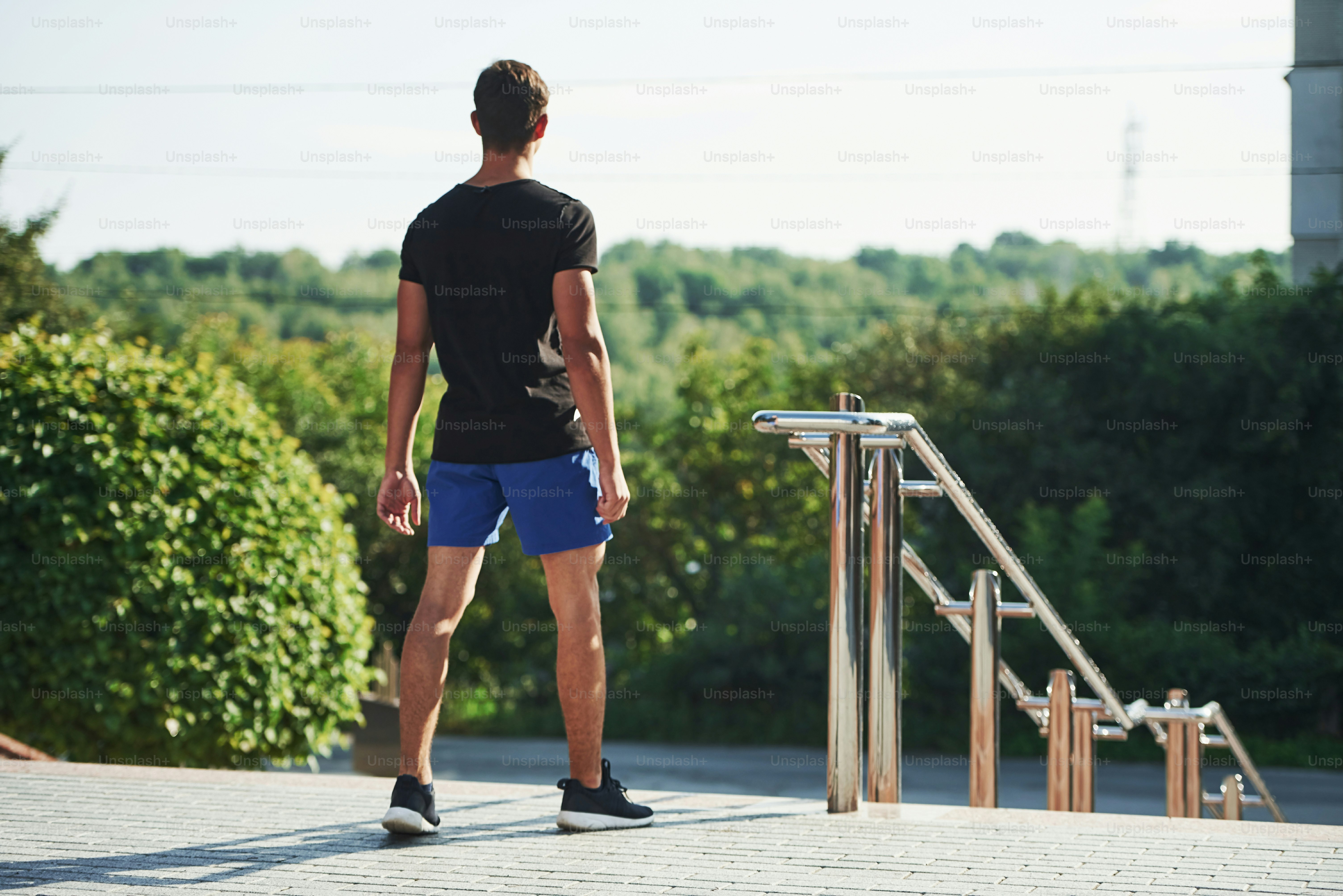 Back view of young man that stands near the railings and looks far away ...