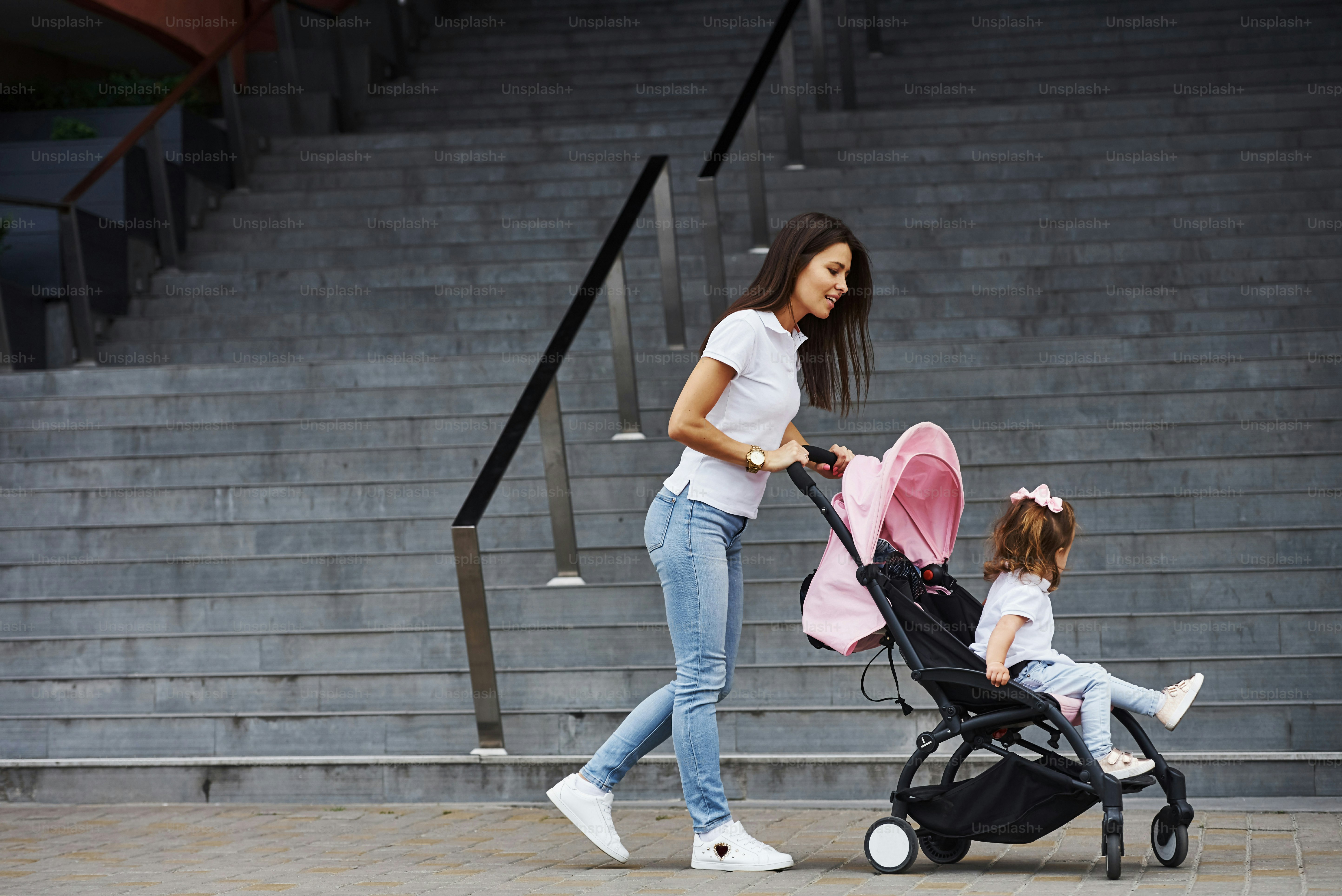 Pretty young mother and her little daughter in pink pram have walk in the city.