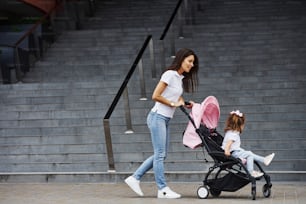 Pretty young mother and her little daughter in pink pram have walk in the city.