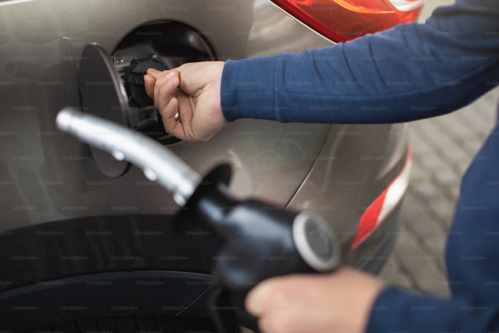 Close up cropped image of male hands, holding filling gun, and opening fuel tank of his luxury car, ready to refueling the car at petrol station.