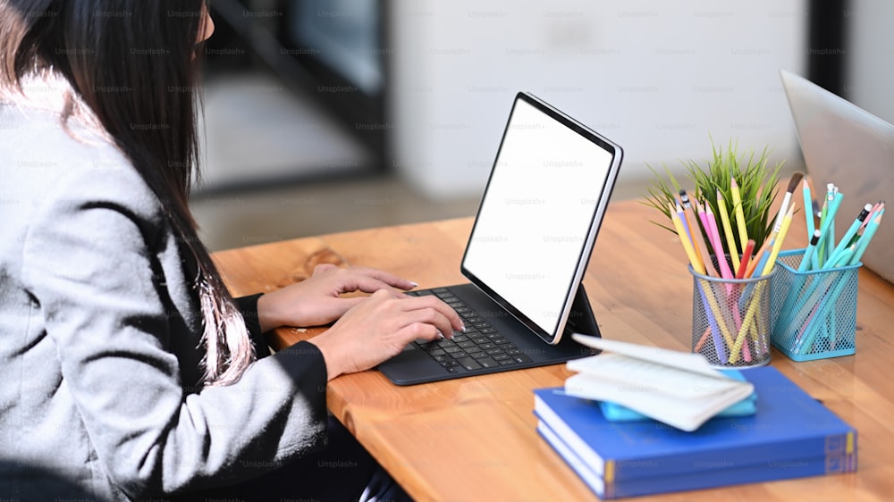 Side view of young female creative designer working with tablet computer on wooden office desk.