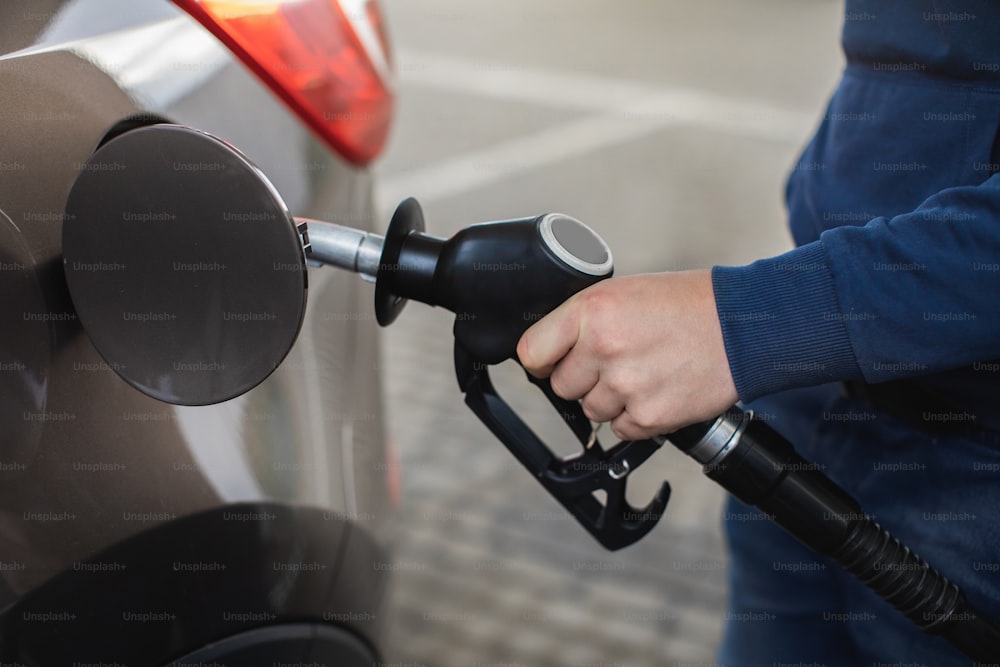 ガソリンスタンドで車の中でガソリン燃料を汲み上げる男の手の接写。自動車にガソリンまたはガソリンが注入される